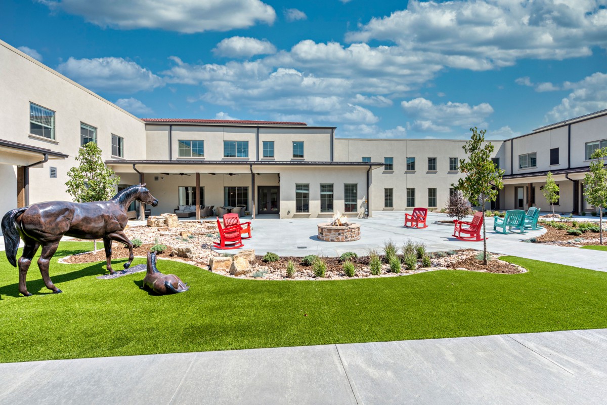 A modern building with an outdoor patio area featuring sculptures and red chairs.