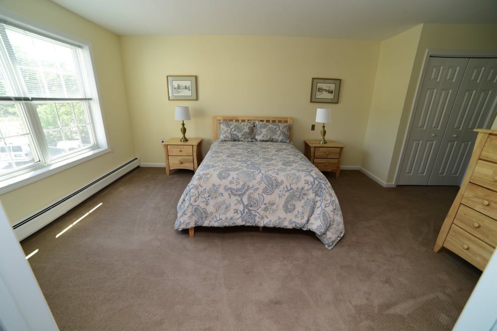 A comfortable bedroom with a neatly made bed, nightstands, lamps, and a carpeted floor.