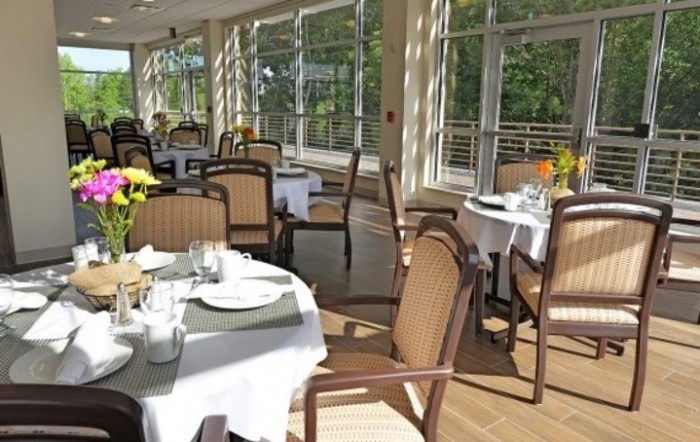 A sunlit dining area with neatly arranged tables and chairs near large windows.