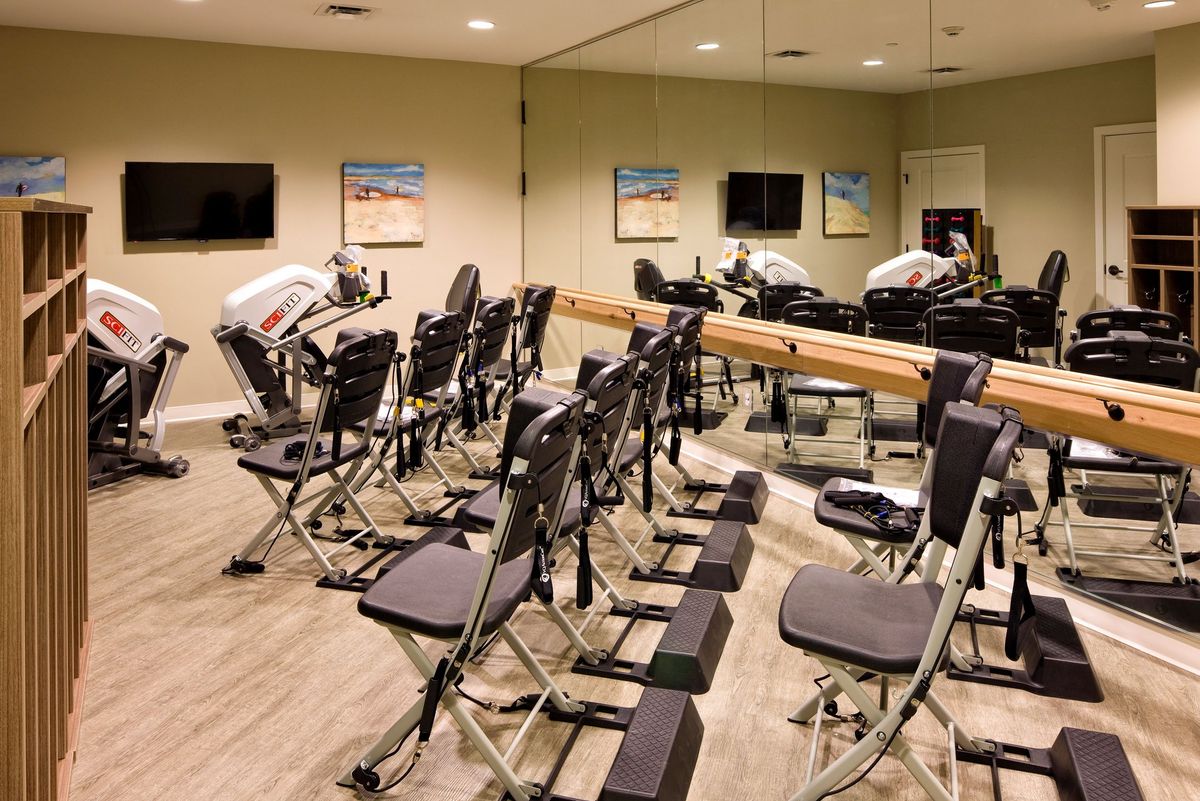 A gym room equipped with exercise machines and chairs, featuring mirrored walls.