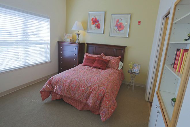 A cozy bedroom featuring a bed with pink bedding, wooden furniture, and floral artwork on the walls.