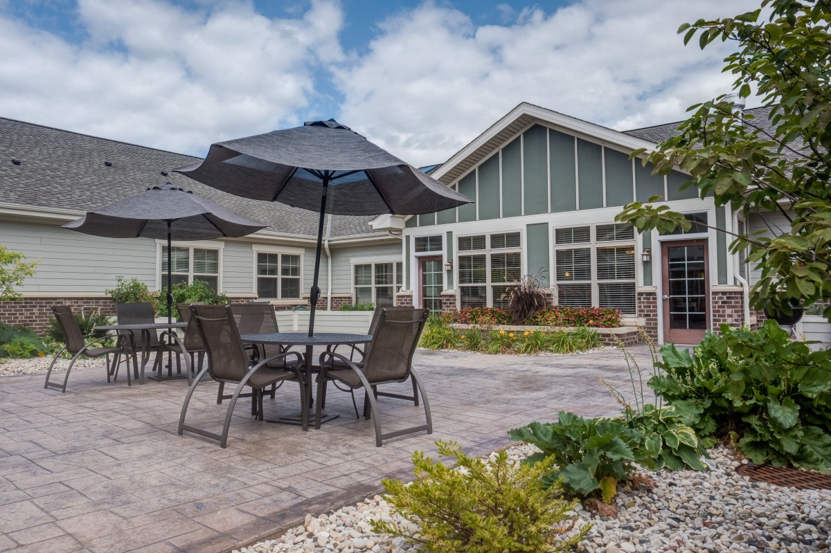 A cozy patio area with tables, chairs, and umbrellas in a garden setting beside a house.