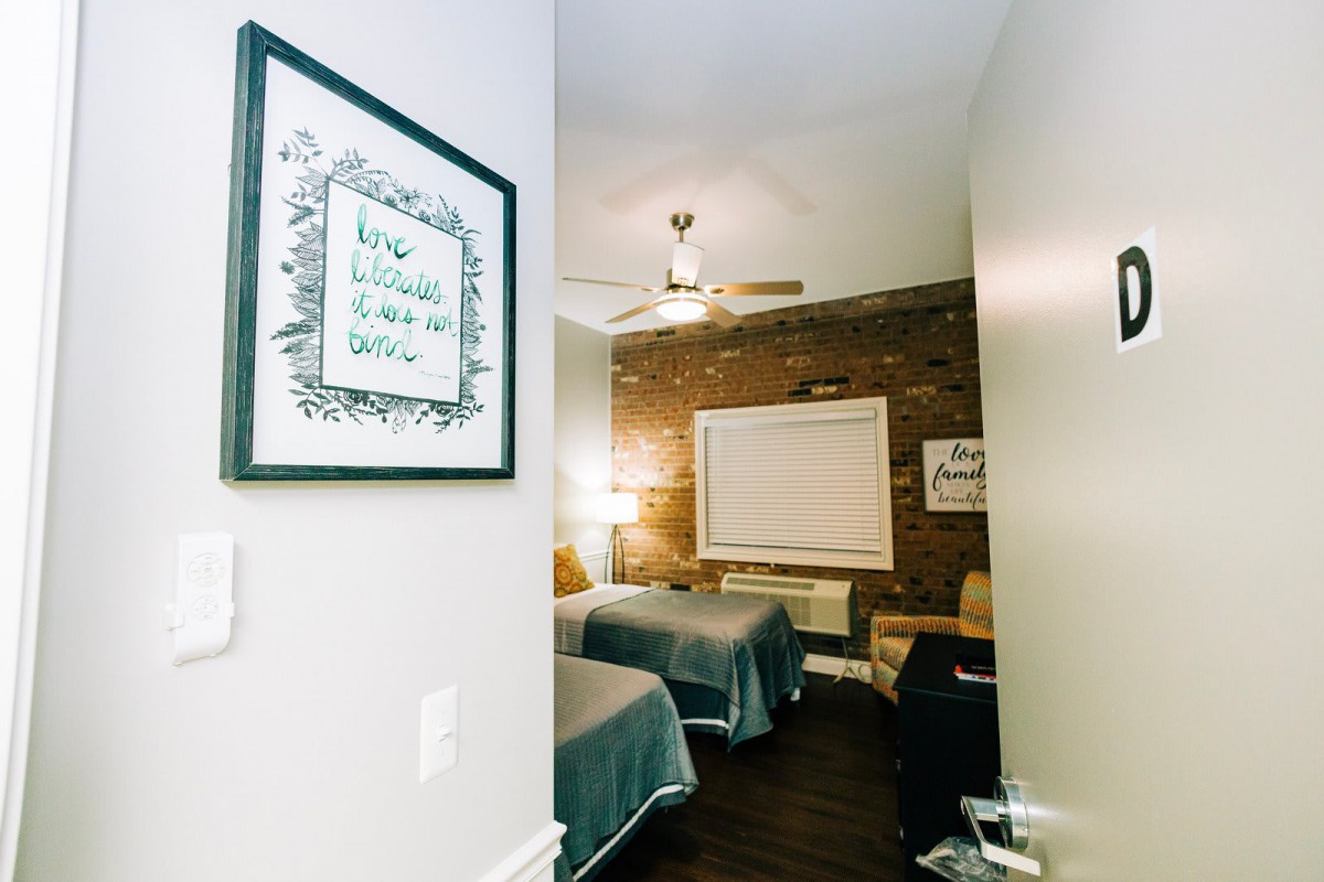 A cozy bedroom with two beds, decorated with a framed artwork and a brick accent wall.