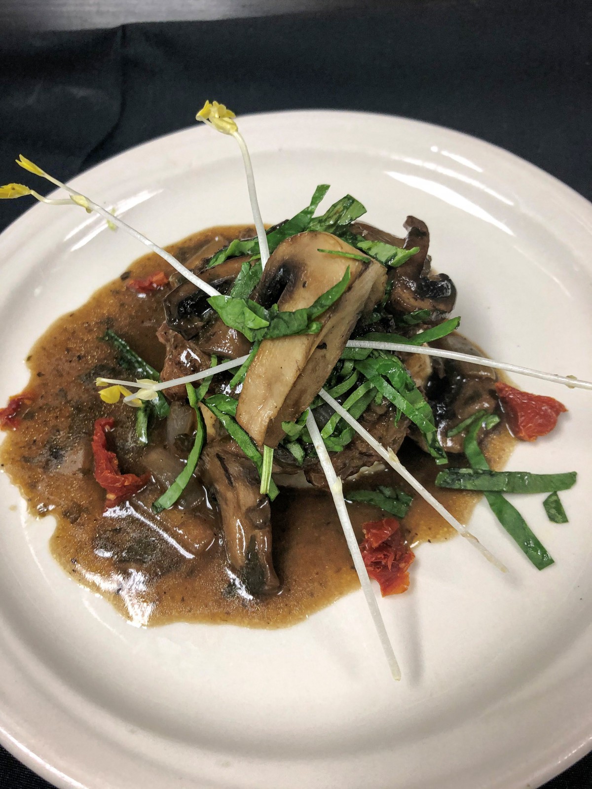 A gourmet dish featuring mushrooms and greens, elegantly arranged with a flavorful sauce on a white plate.