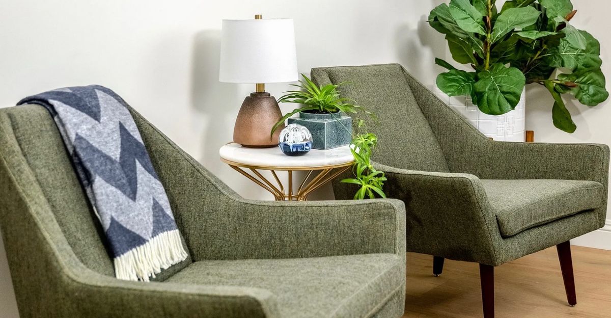 A cozy modern living room setup with green chairs, a round table, decorative plants, and a stylish lamp.