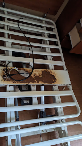 A damaged bed frame with visible rust and an electrical cord on top.