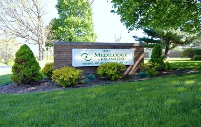 A building sign for The Medilodge of Kalamazoo surrounded by lush greenery and trees.