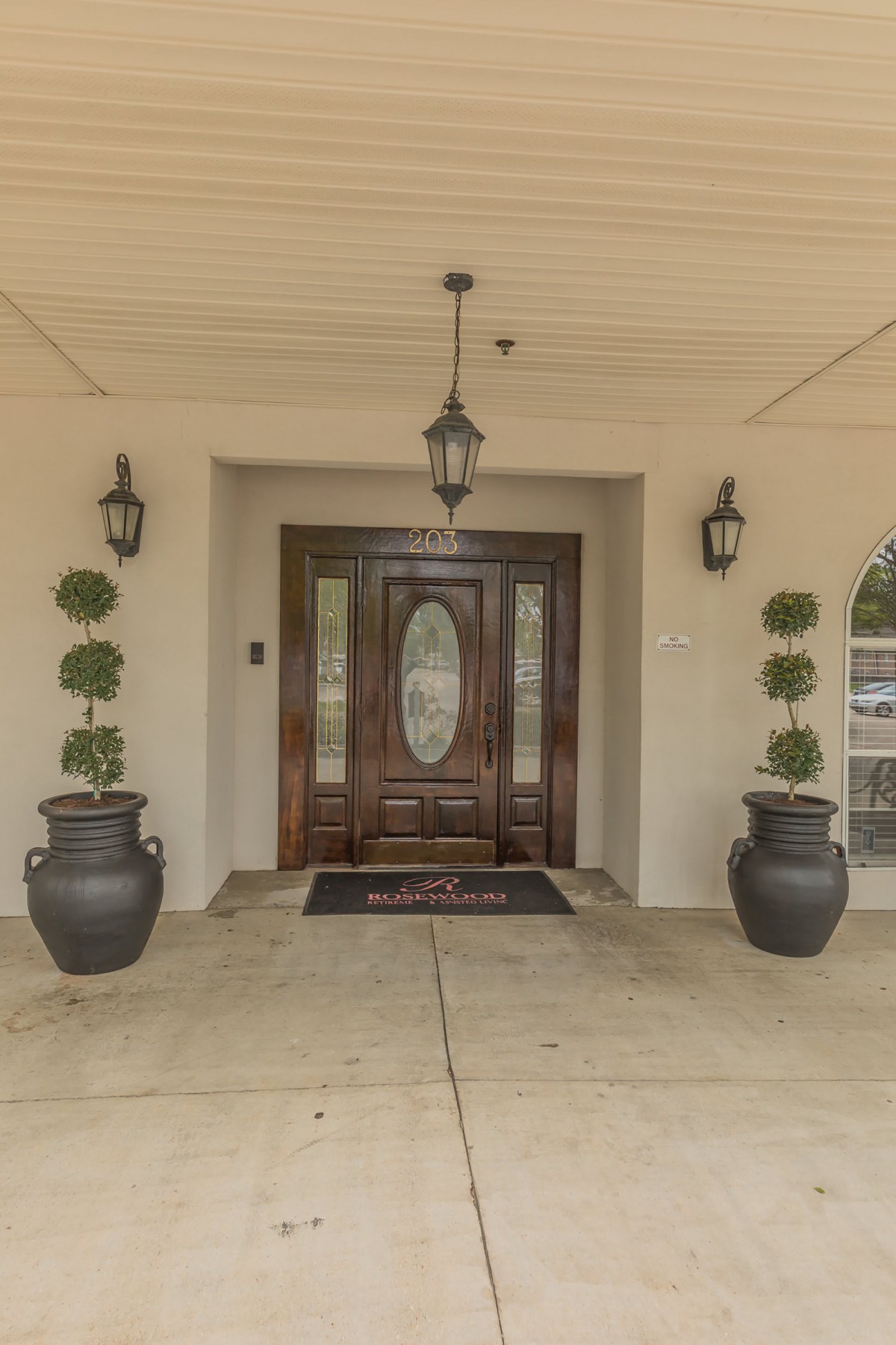 A symmetrical entrance with a wooden front door, flanked by potted plants and lanterns.