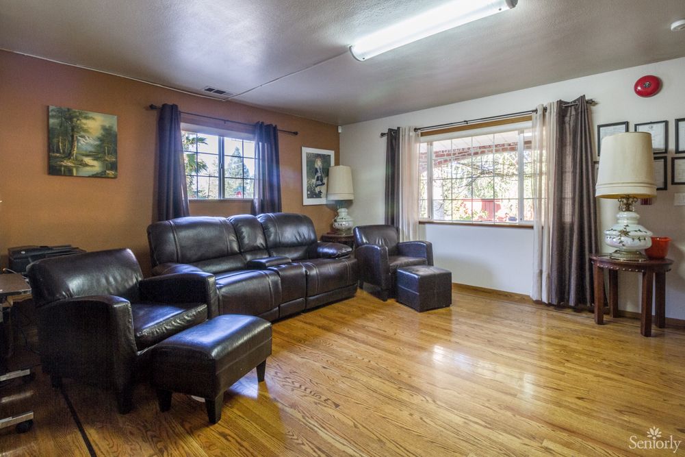 A cozy living room with leather seating and hardwood floors, illuminated by natural light from large windows.