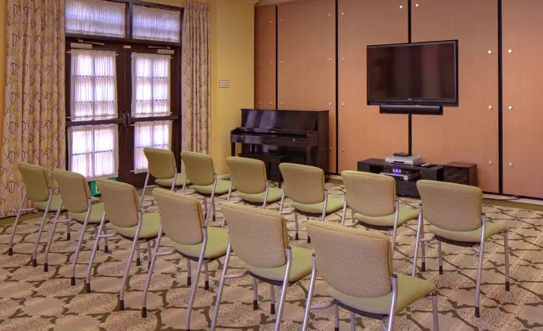 A small conference room with rows of chairs facing a piano and large television.