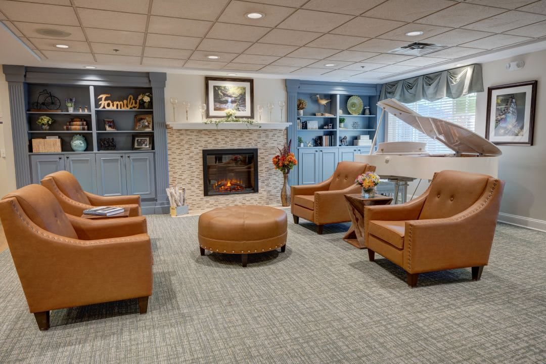 A cozy living room with leather chairs arranged around a central ottoman, featuring a fireplace and built-in shelving.