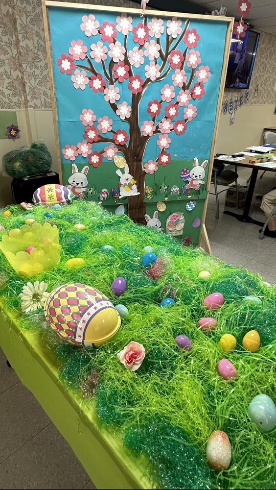 A festive Easter table display featuring colorful eggs, a grassy setup, and bunny decorations with a painted backdrop.