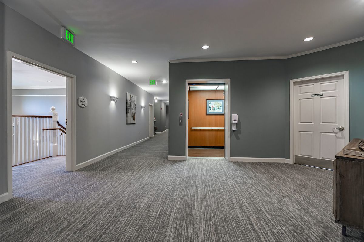A modern hallway with an elevator and carpeted flooring.