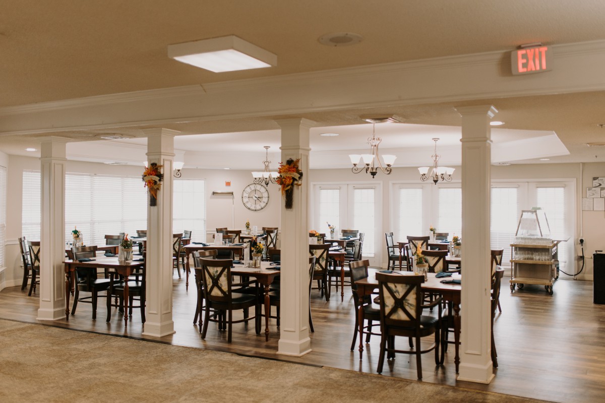 An empty dining room with neatly arranged tables and chairs, featuring decorative columns.