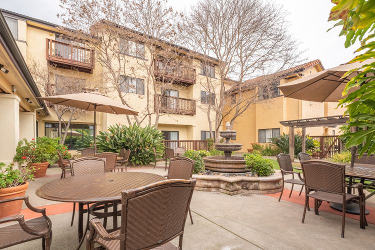 A cozy outdoor patio area in an apartment complex with seating, umbrellas, and a central fountain.