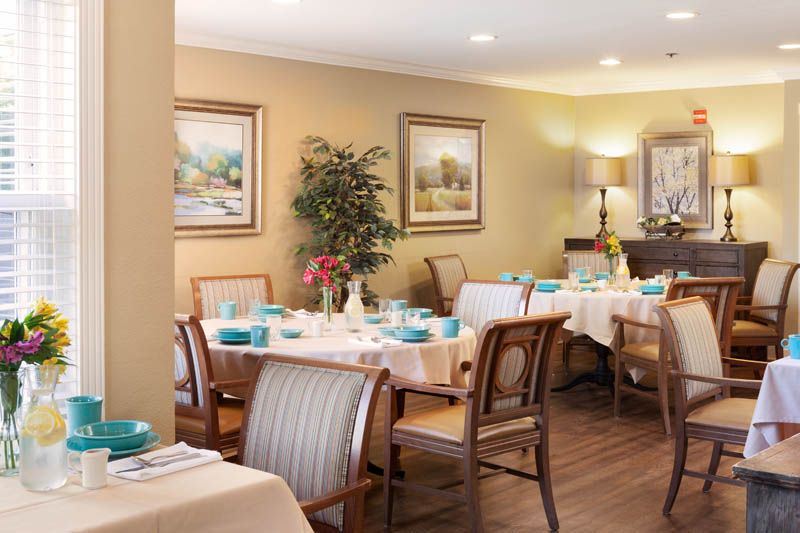 A cozy dining room with neatly arranged tables set for a meal, decorated with artwork and plants.