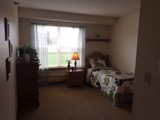 A cozy bedroom with a single bed, dresser, and a lamp near the window.