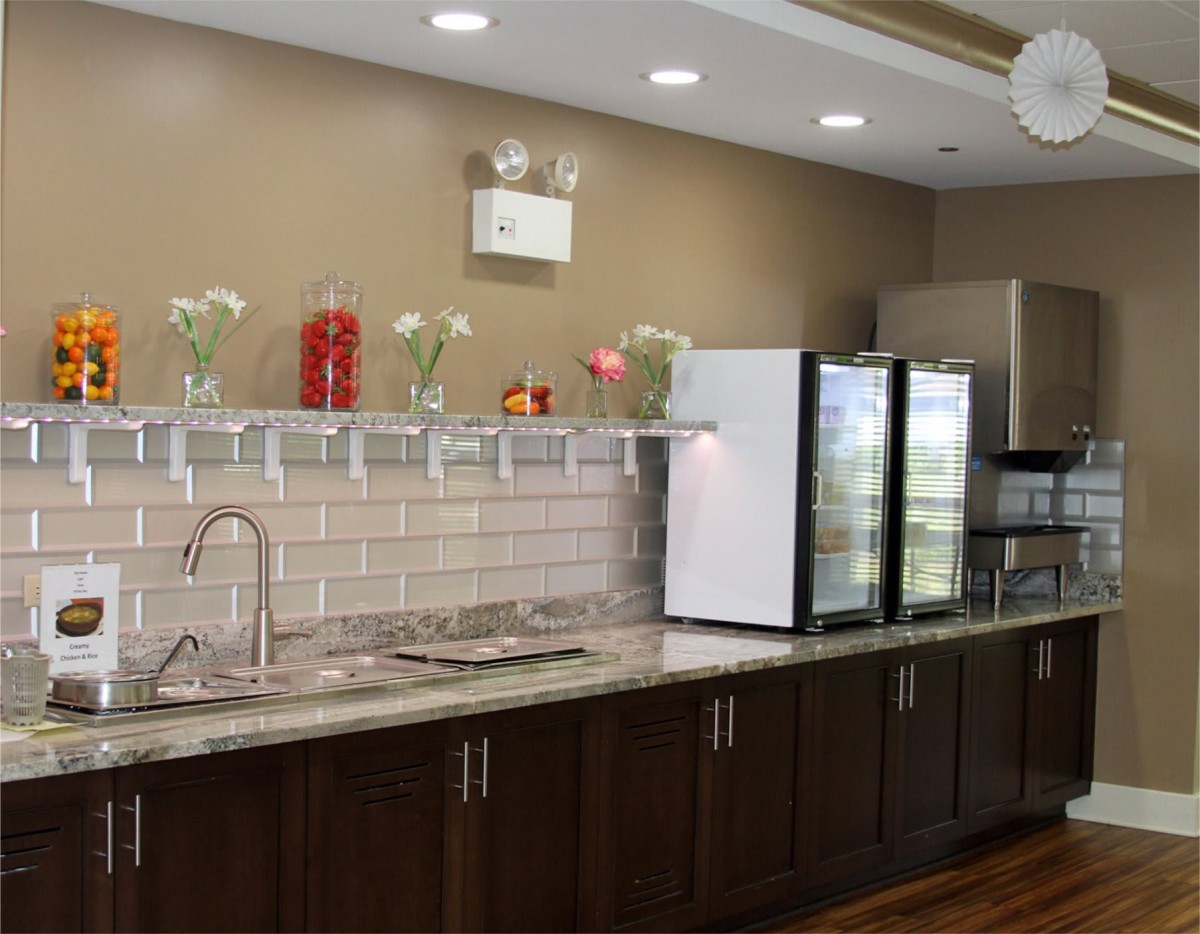 A modern kitchen area with dark wood cabinets, a sink, and a refrigerator, adorned with flowers and well-lit.