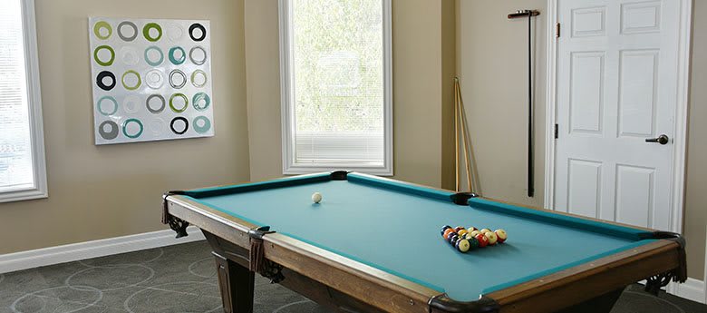 A pool table set up in a game room with cue sticks resting against the wall.
