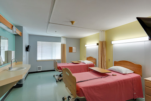 A well-lit hospital patient room featuring two beds with pink linens.
