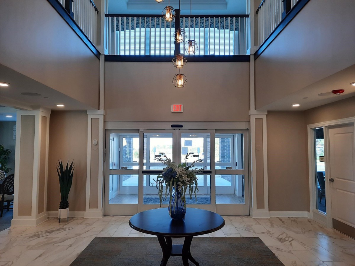 A modern lobby with a central round table, decorative plant, and chandelier lighting.