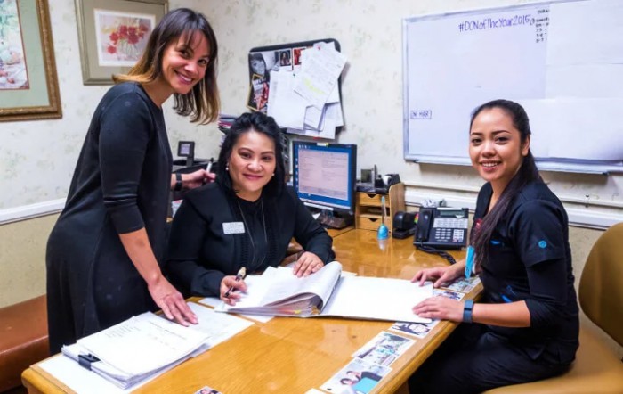 Three women collaborating in an office setting, reviewing documents at a desk.
