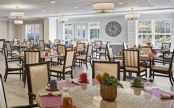 A bright and neatly arranged dining area with multiple tables and chairs, decorated with colorful table settings.