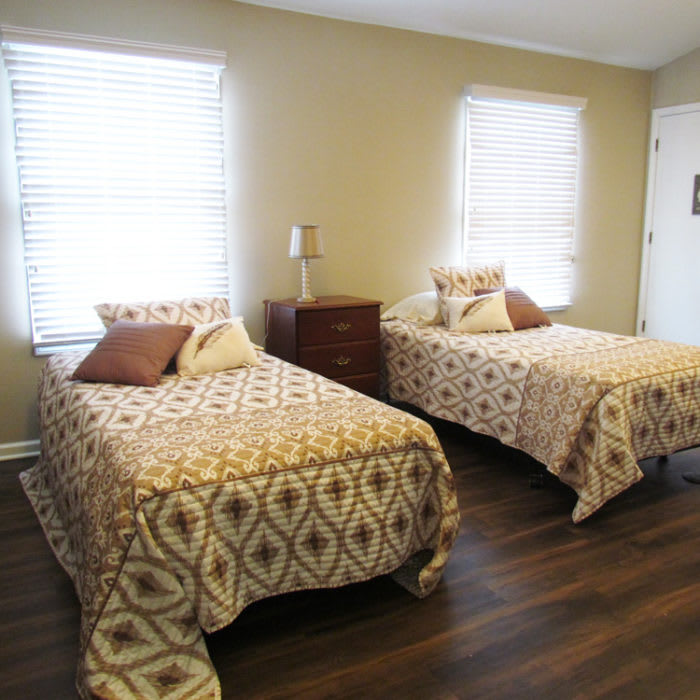 A cozy bedroom with twin beds featuring patterned blankets and pillows, complemented by wooden flooring and natural light from the windows.