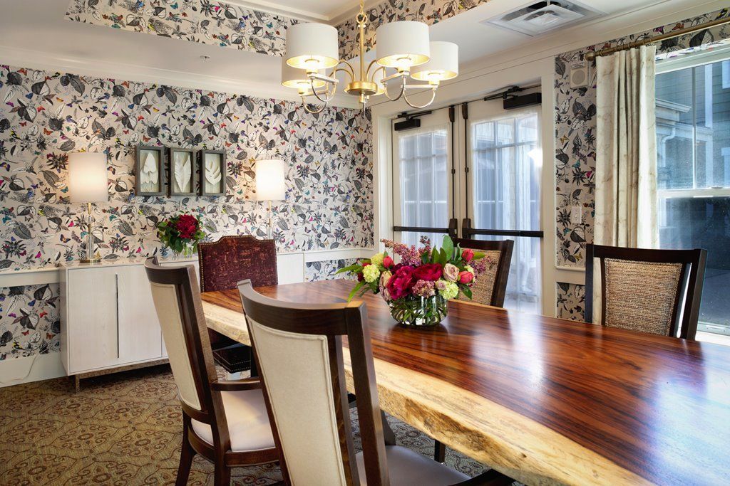 A beautifully decorated dining room featuring a wooden table, floral wallpaper, and elegant lighting.