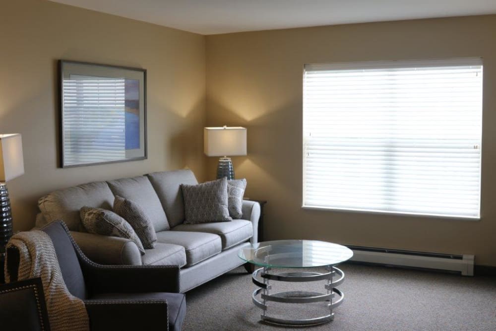 A cozy living room with a gray couch, modern coffee table, and a lamp by the window.