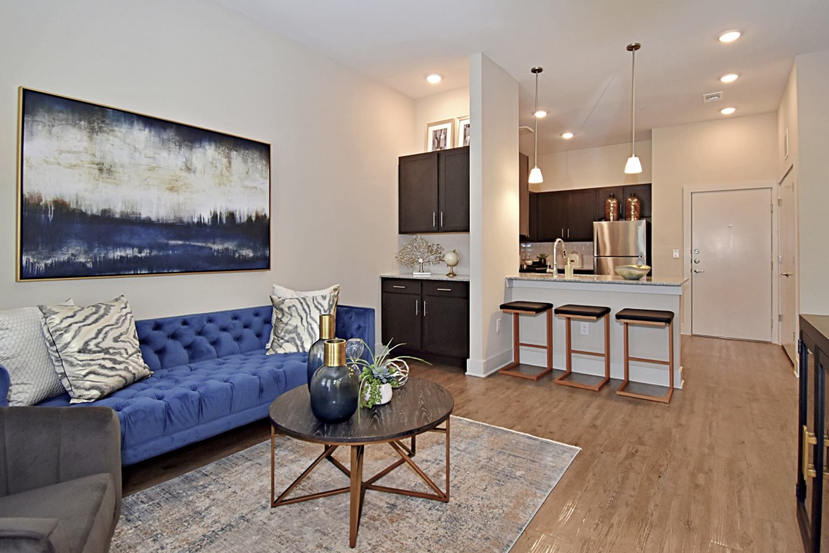 A modern living room with a blue sofa, coffee table, and adjoining kitchen with barstools.