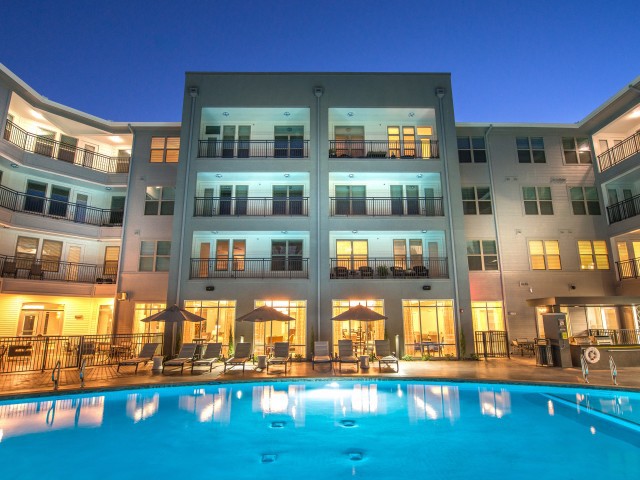 Illuminated apartment building with a swimming pool at night.
