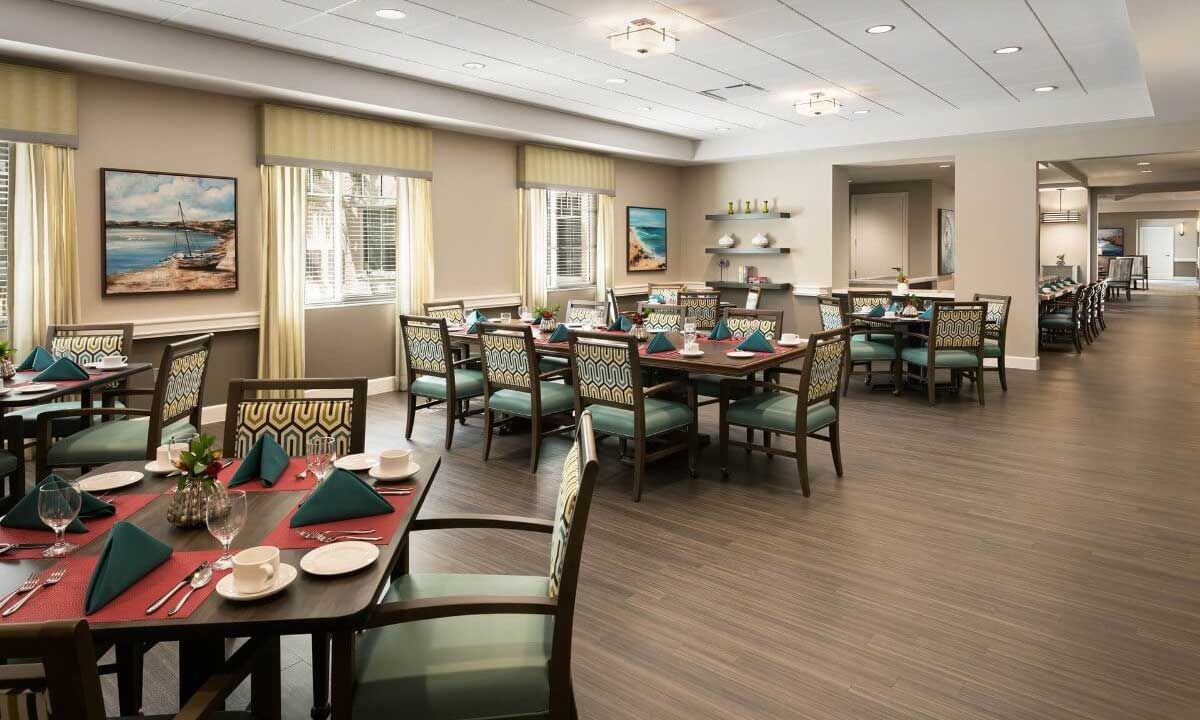 A well-decorated dining area with neatly arranged tables and chairs, featuring large windows and elegant lighting.