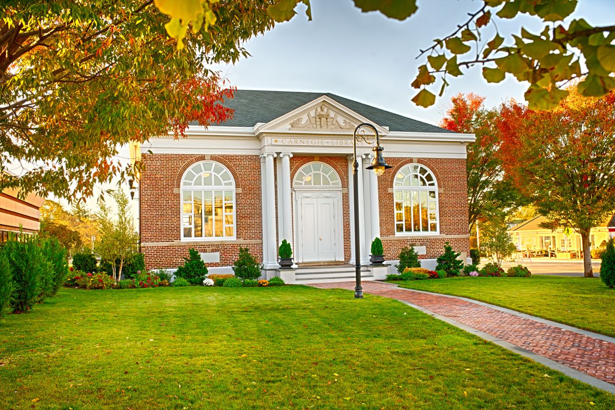 A quaint brick library building surrounded by autumn foliage.