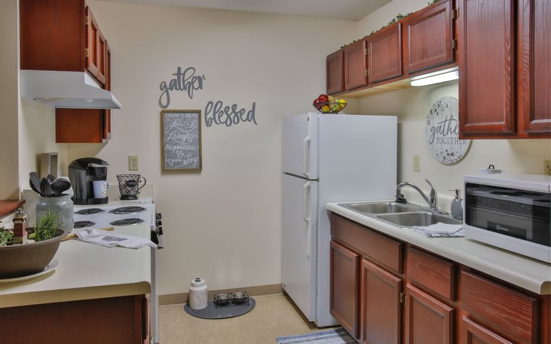 A cozy kitchen with wooden cabinets, a white refrigerator, and stove, featuring wall decor with inspirational words.