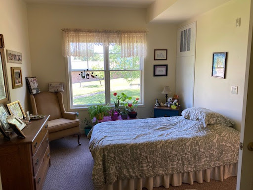 A cozy bedroom featuring a neatly made bed, comfortable chair, and bright natural light coming through the window.