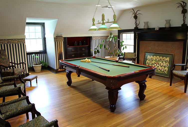A cozy billiard room featuring a classic pool table with cues set on top, illuminated by an overhead light fixture.