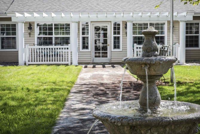 A peaceful garden with a stone fountain leading to a charming house.