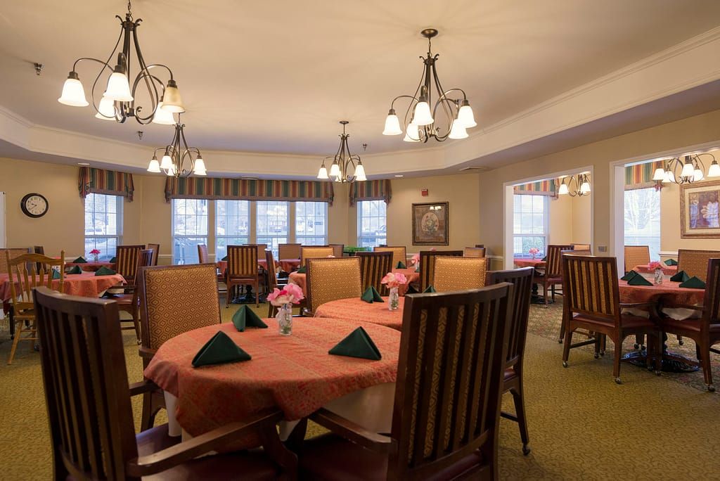 A well-decorated dining room with multiple tables set for a meal, featuring chandeliers and floral centerpieces.