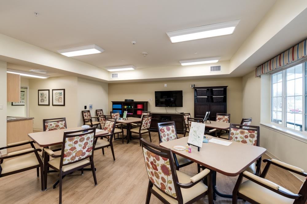 A well-lit room with multiple tables and chairs, equipped with a TV screen.