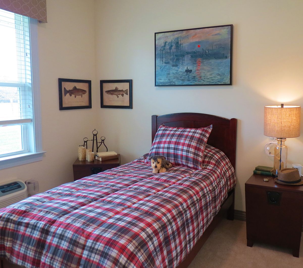 A cozy bedroom with a single bed featuring plaid bedding, decorated with wall art and a bedside lamp.