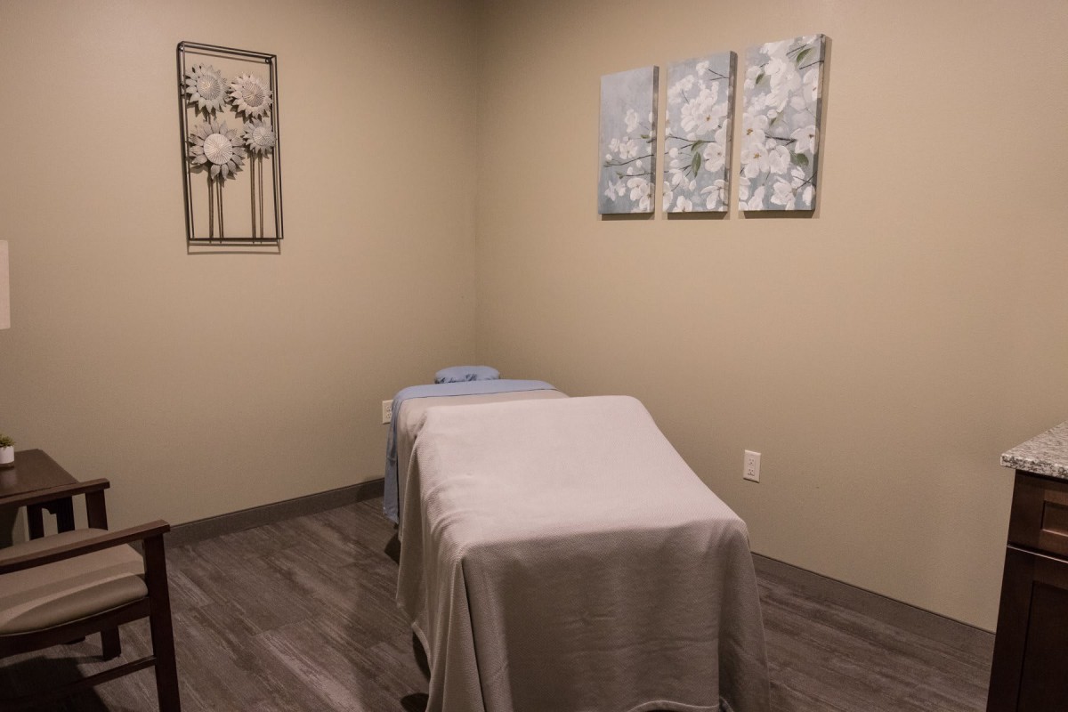 A tranquil massage room with a neatly made treatment table and calming wall art.