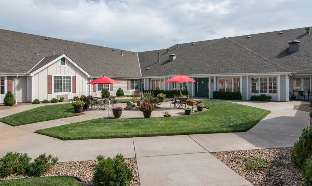 A well-maintained residential building with a spacious green lawn and red umbrellas on the patio.