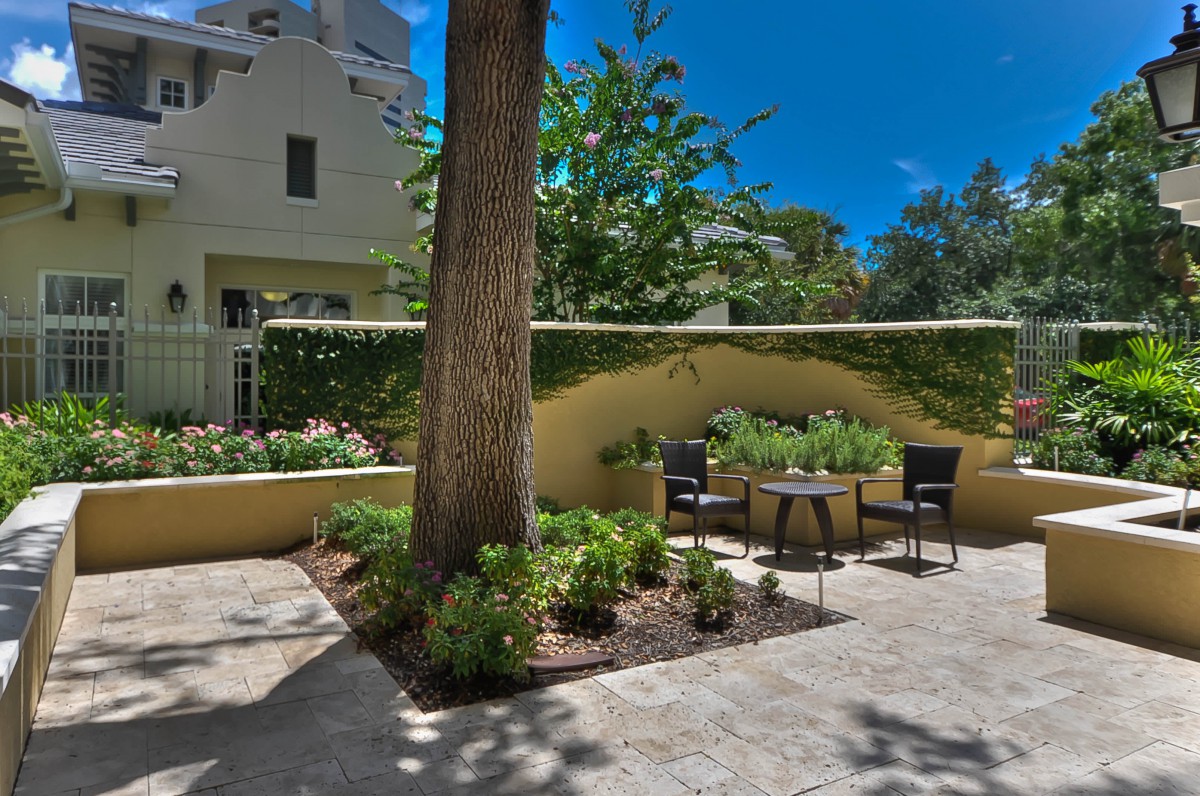 A tranquil garden patio with chairs and a table surrounded by lush greenery.