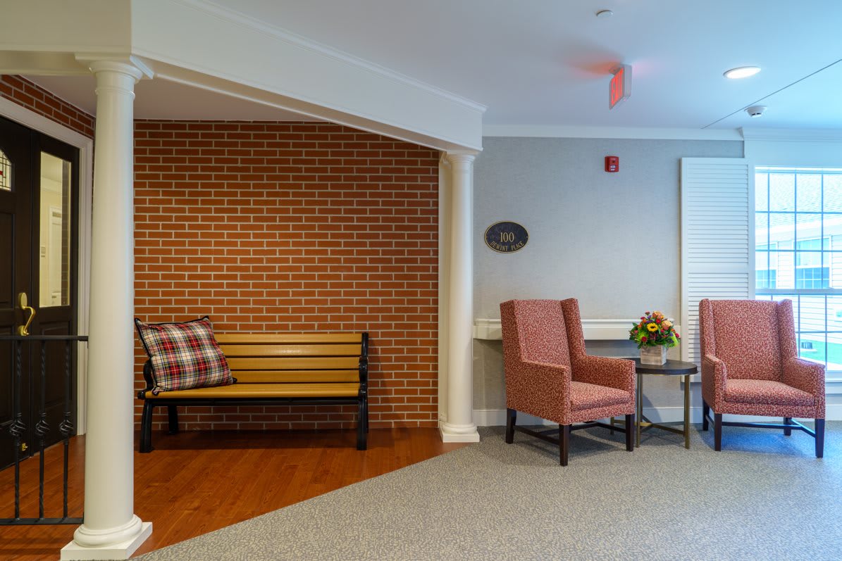 A cozy seating area featuring armchairs, a bench with a plaid pillow, and a small table against a brick wall.