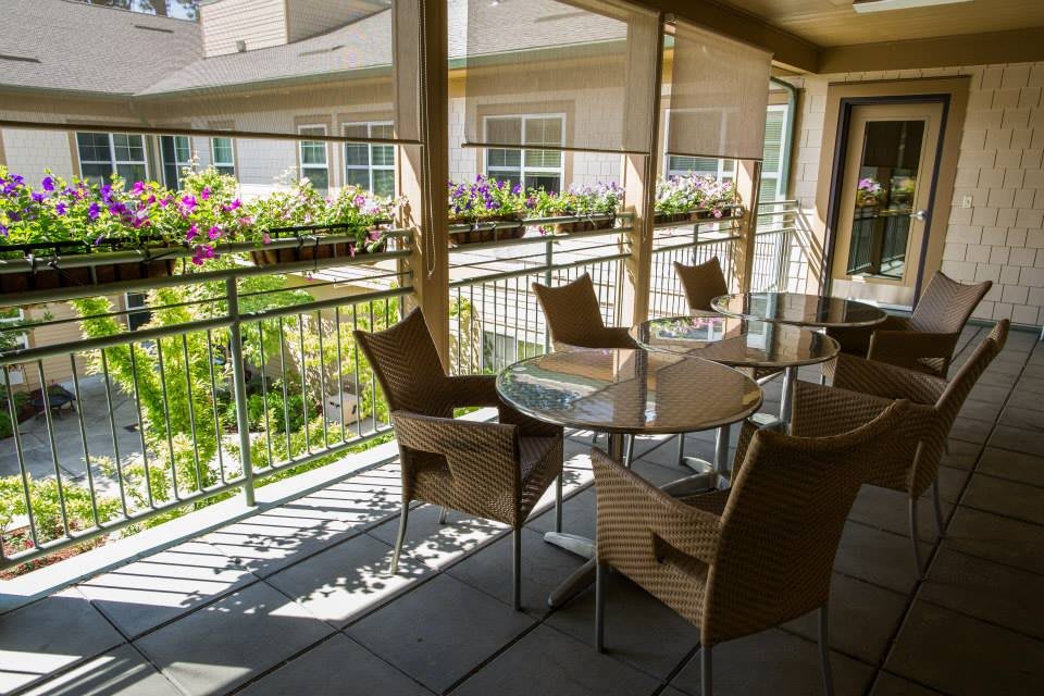 A sunlit patio with wicker chairs and a glass table overlooking a garden.