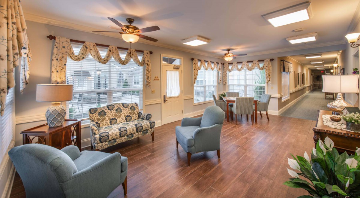 A cozy living space featuring multiple seating options, wood flooring, and ample natural light from large windows.