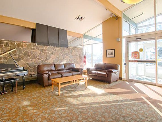A cozy lobby with leather sofas and a coffee table, warmly illuminated by natural light streaming through large windows.