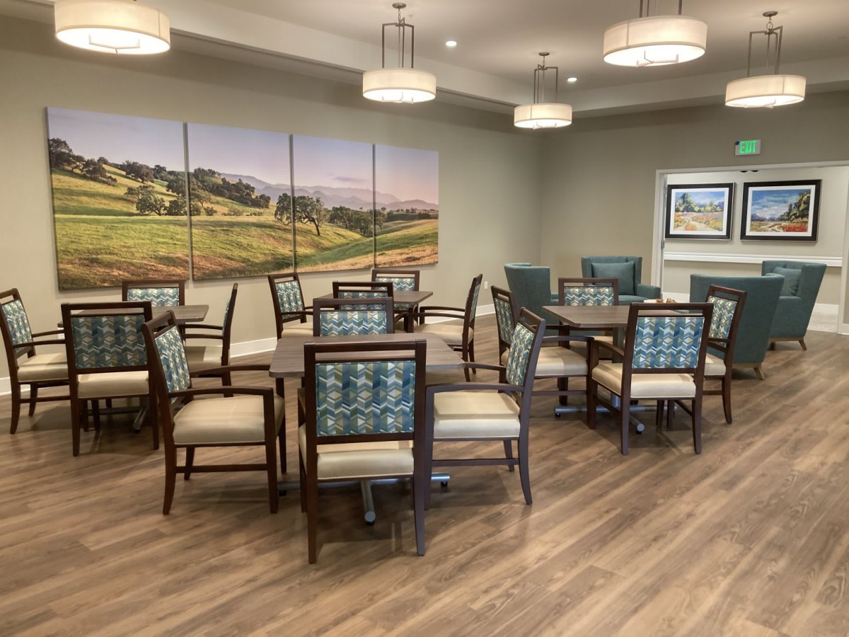 A modern dining room with neatly arranged tables and chairs, featuring elegant lighting and wall art.
