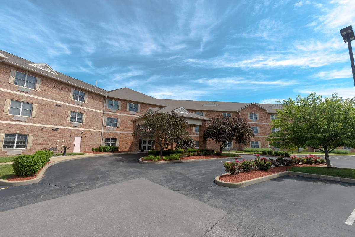A three-story residential building with landscaped surroundings under a blue sky.